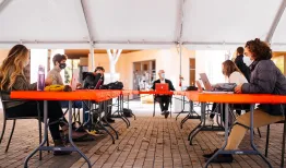 Students and a professor sitting at makeshift desks under a large outdoor tent for outdoor instruction. | Credit: Elena Zhukova.