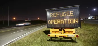 A car drives by a sign on a road displaying "Refugee Operation"
