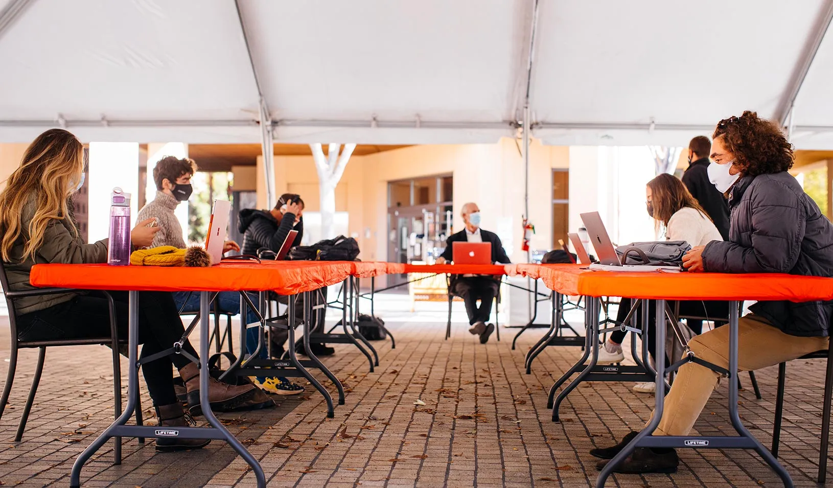 Students and a professor sitting at makeshift desks under a large outdoor tent for outdoor instruction. | Credit: Elena Zhukova.
