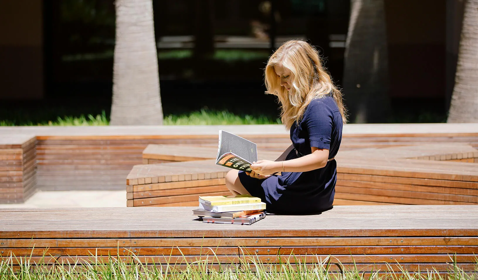 A student sits reading in McCoy Courtyard next to a stack of books. Photo by Tricia Seibold