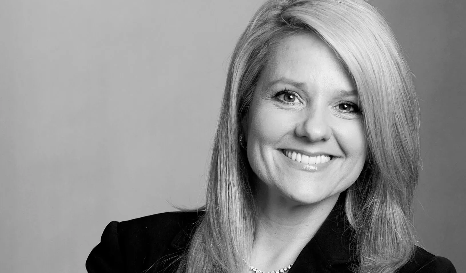 Black and white portrait of Gwynne Shotwell smiling at the camera on a dark grey background. Courtesy of Gwynne Shotwell