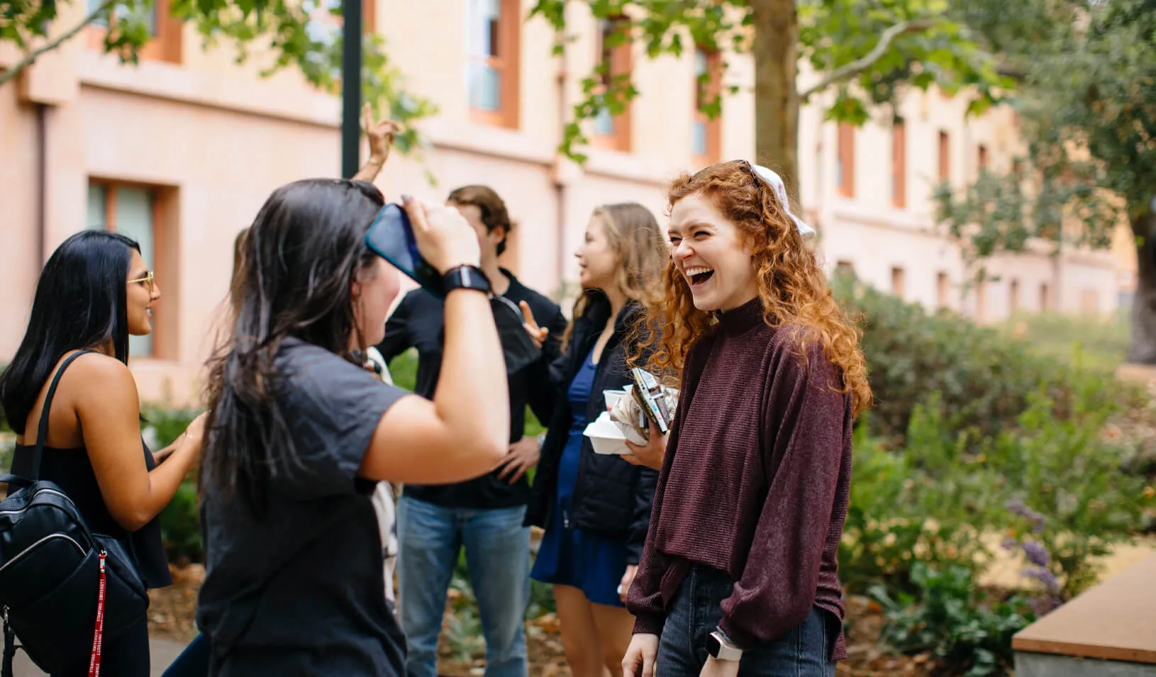 Three students standing outside of Schwab Residential Center, laughing and high-fiving. Photo by Elena Zhukova.