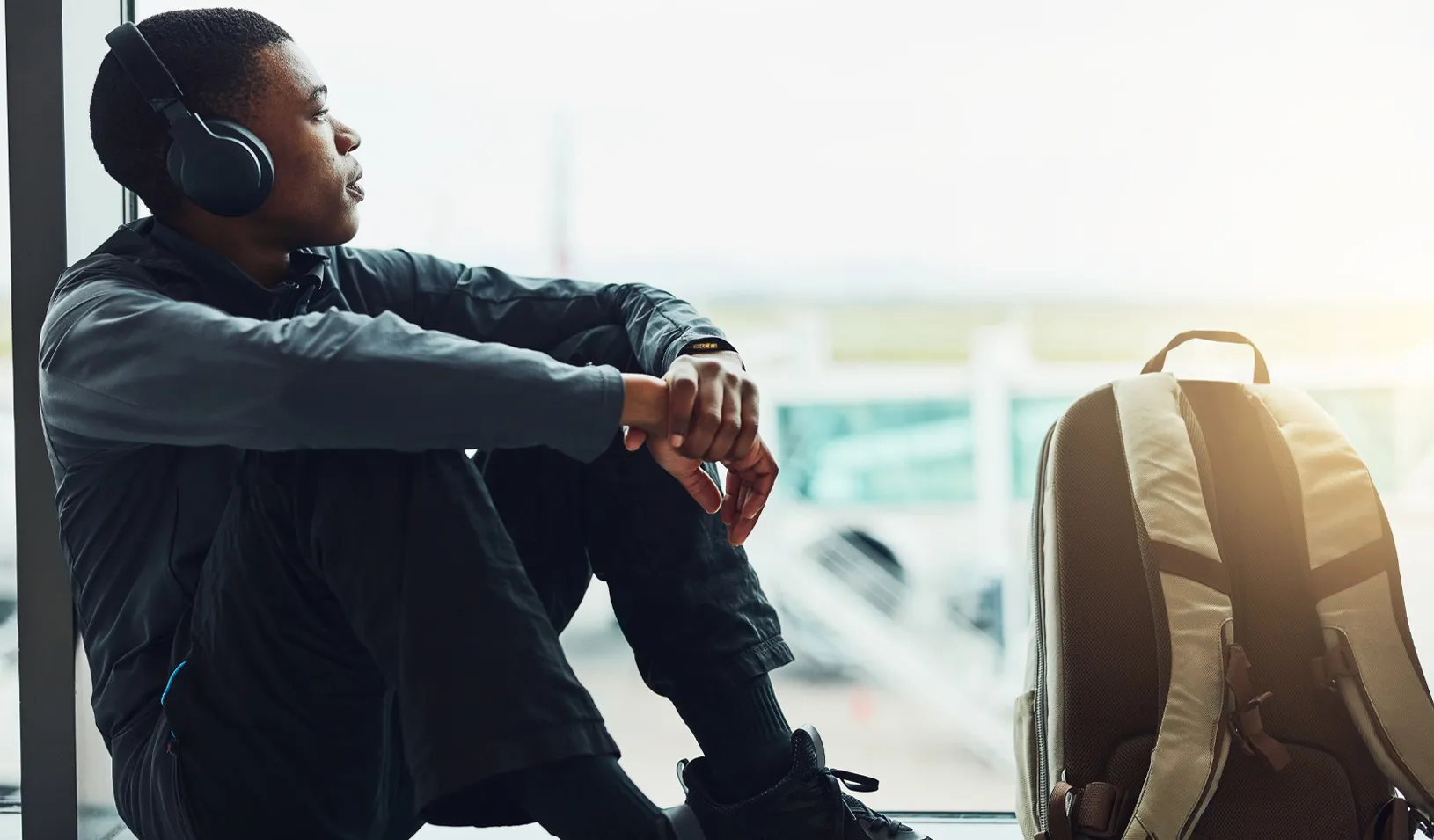 Shot of a young man with headphones on, sitting at the airport waiting for departure. Credit: iStock/PeopleImages