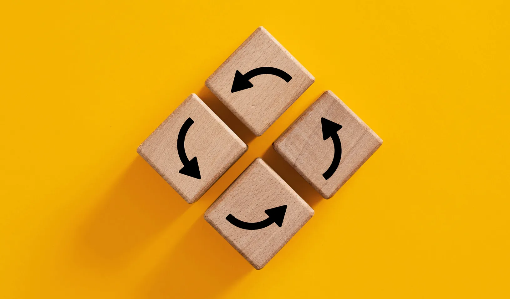 Photo of 4 wood blocks on a yellow background, with arrows on them indicating a circular, repeating pattern. Credit: iStock/cagkansayin