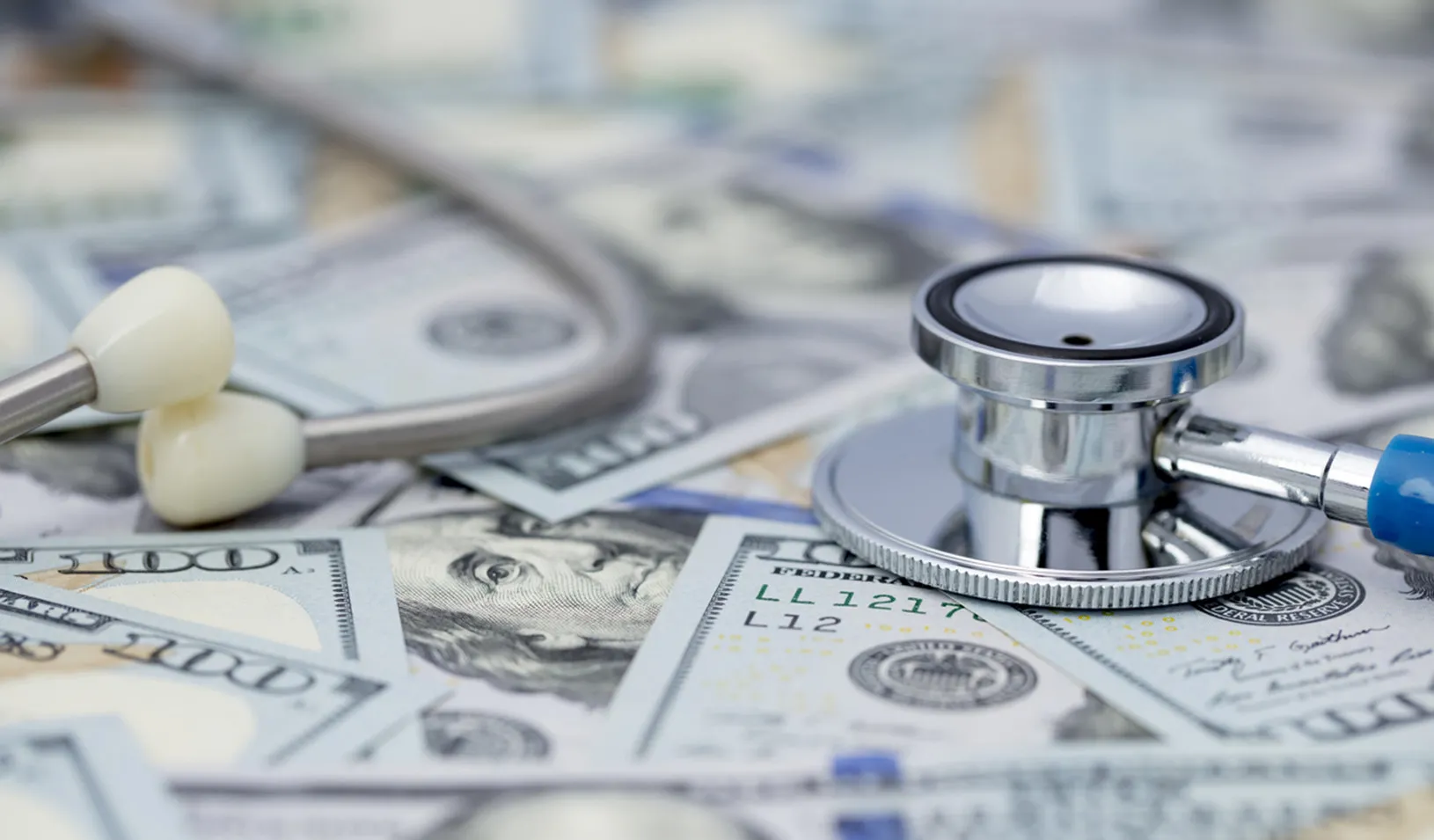 A stethoscope sitting on a pile of scattered one hundred dollar bills. iStock/Viorika