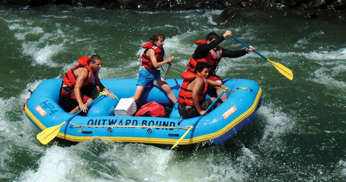 Four young adults paddle down a rapid in an Outward Bound raft.