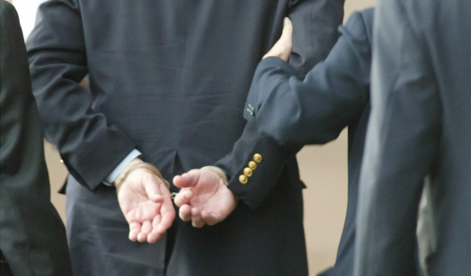 man in suit with hands cuffed behind back | Reuters/Richard Carson
