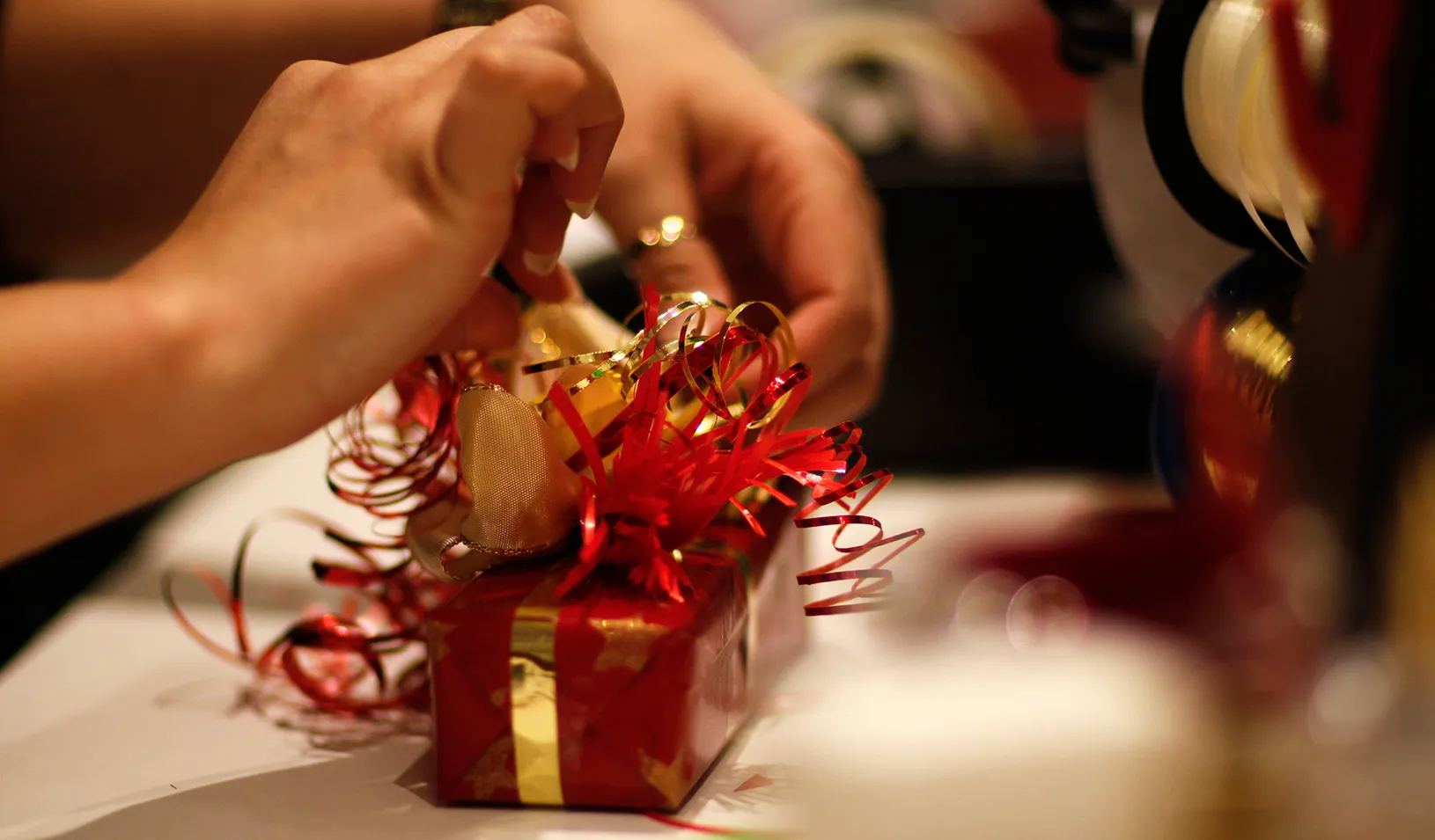 Someone adds ribbon to a holiday gift