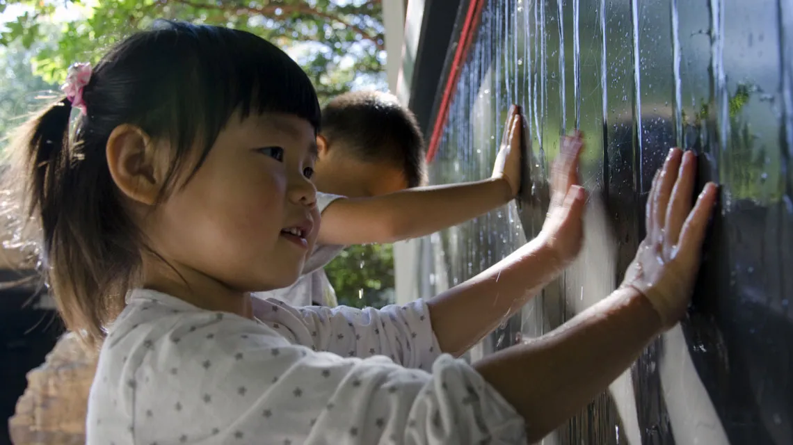 A little girl plays with and learns about water as it trickles down the wall.